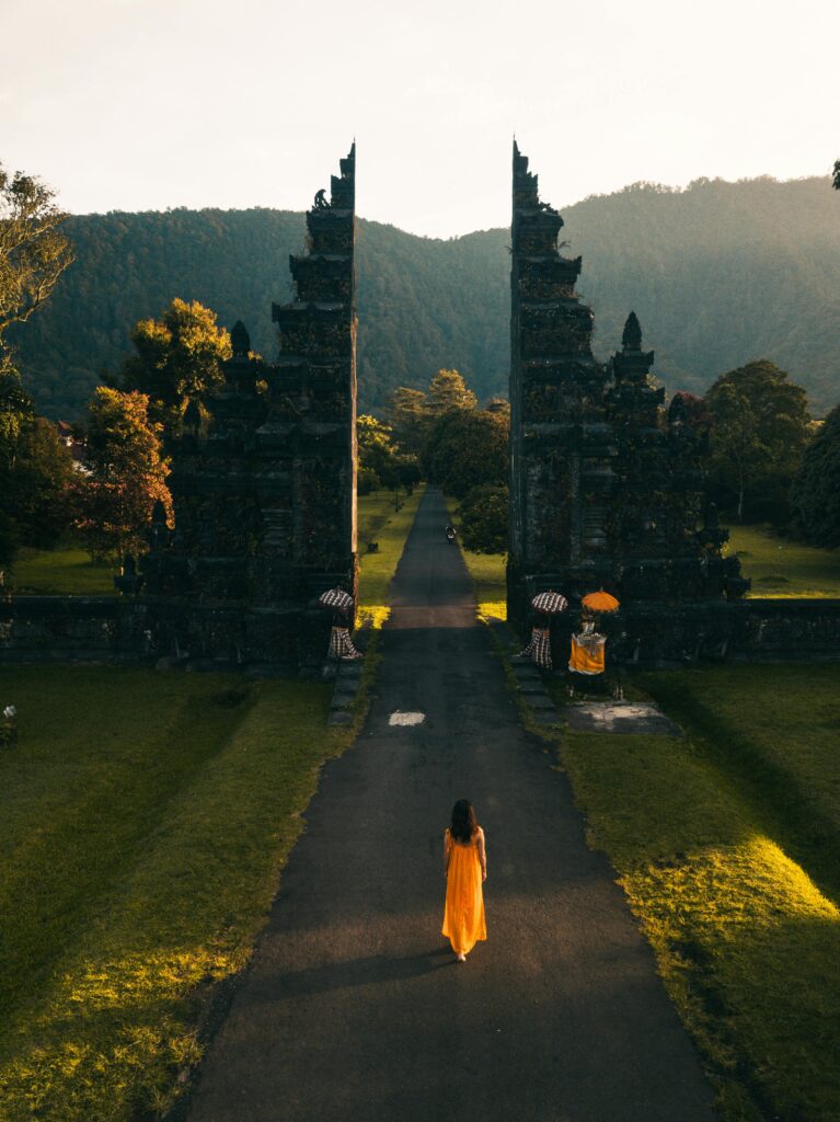 pexels-photo-2499699-2499699 Aerial view of a woman in orange dress walking towards Bali Handara Gate at sunrise in Indonesia.