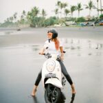 Woman on a scooter enjoying a sandy beach in Bali, Indonesia with palm trees in the background.
