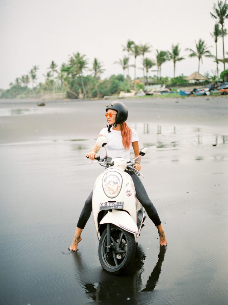 Woman on a scooter enjoying a sandy beach in Bali, Indonesia with palm trees in the background.
