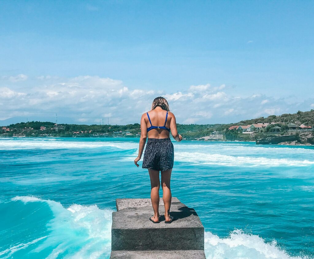 A woman stands on a pier, embracing the tropical ocean view in Bali, Indonesia. Perfect summer escape.
