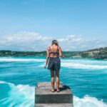 A woman stands on a pier, embracing the tropical ocean view in Bali, Indonesia. Perfect summer escape.