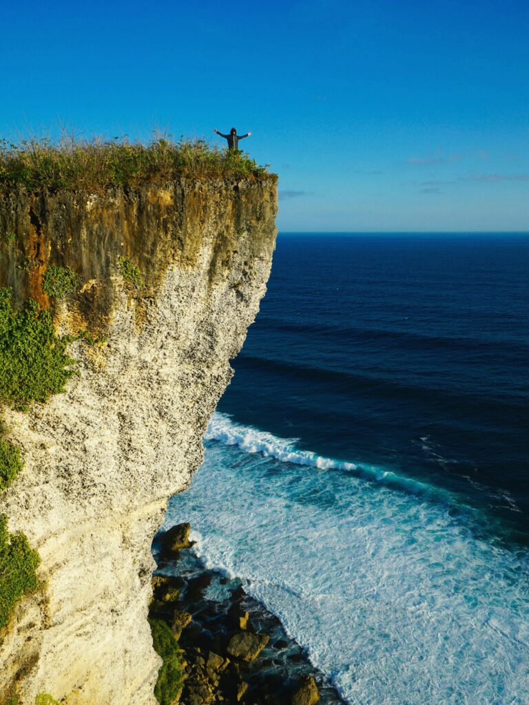 Stunning view of Uluwatu cliff with the ocean waves crashing below under a clear blue sky.